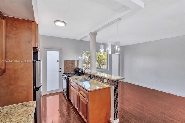 kitchen with gas stove, sink, light stone counters, stainless steel fridge, and pendant lighting