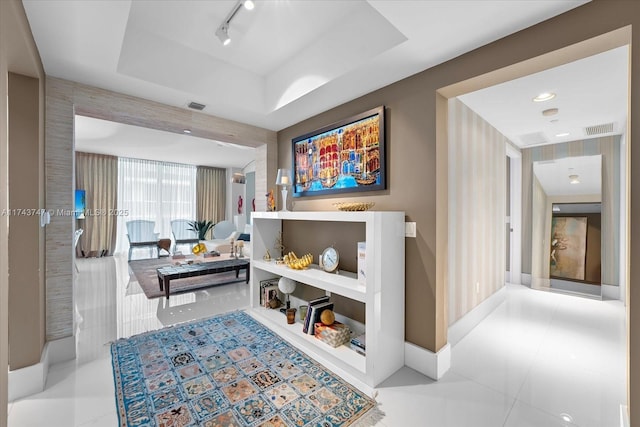 corridor featuring a raised ceiling, track lighting, and tile patterned floors