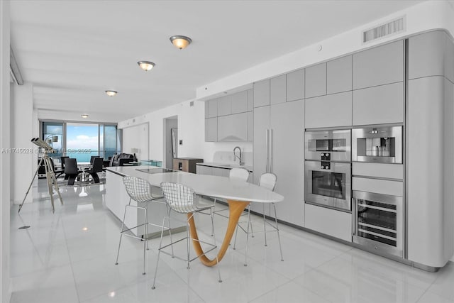 kitchen with sink, a breakfast bar area, gray cabinetry, double oven, and a kitchen island