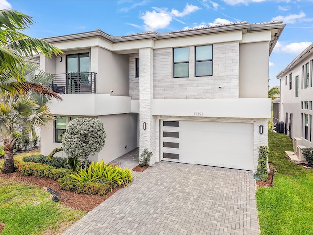 view of front of home with decorative driveway, stucco siding, a balcony, and central AC unit