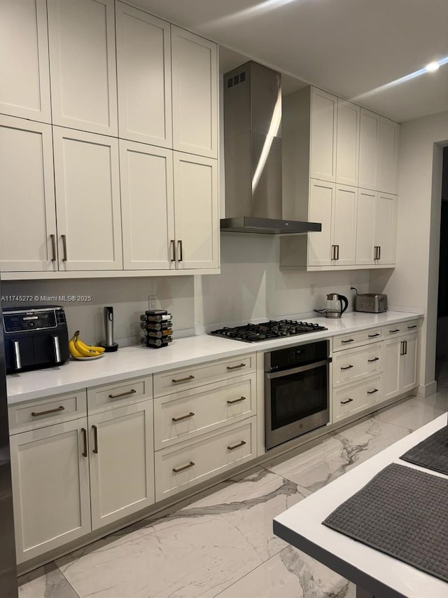 kitchen featuring oven, gas stovetop, marble finish floor, light countertops, and wall chimney exhaust hood