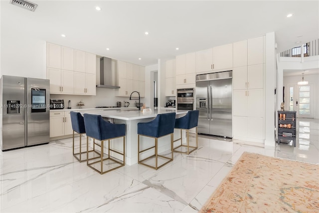 kitchen featuring marble finish floor, a kitchen bar, visible vents, appliances with stainless steel finishes, and wall chimney exhaust hood