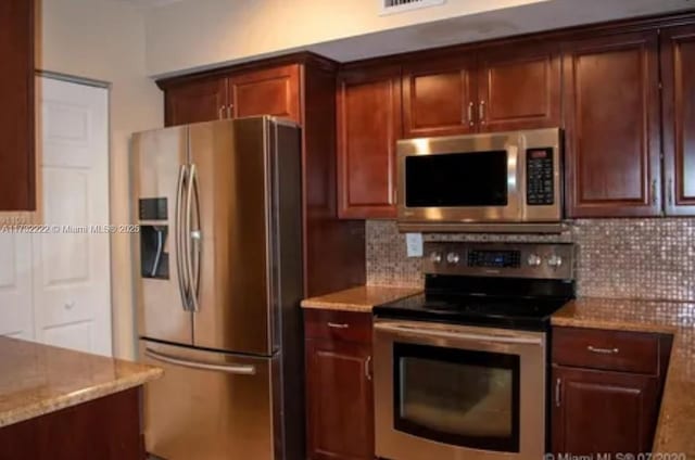 kitchen with light stone countertops, appliances with stainless steel finishes, and backsplash