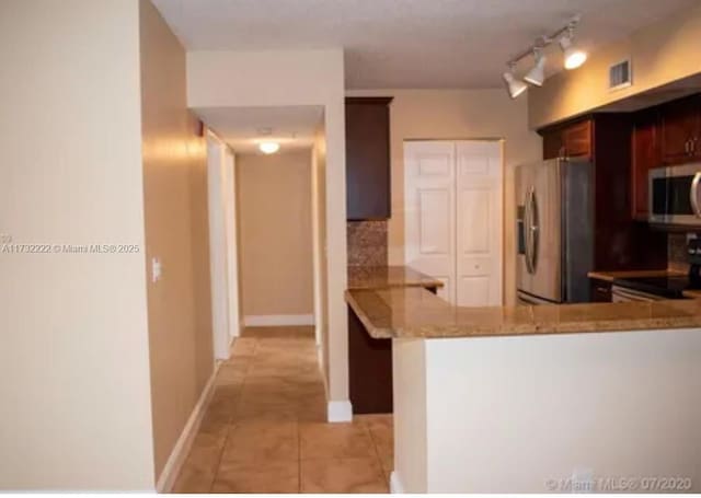 kitchen with stainless steel fridge, stove, light stone counters, light tile patterned flooring, and kitchen peninsula