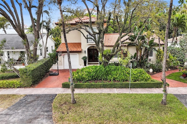 mediterranean / spanish house featuring driveway, a front yard, a tile roof, and stucco siding