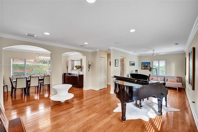 sitting room featuring light wood-style floors, arched walkways, ornamental molding, and baseboards