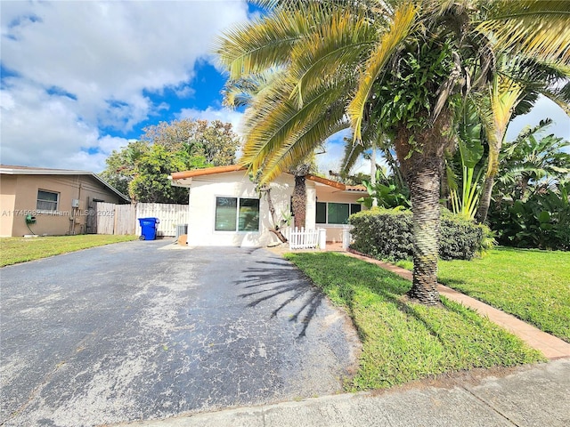 view of front of home featuring a front lawn, fence, aphalt driveway, and stucco siding