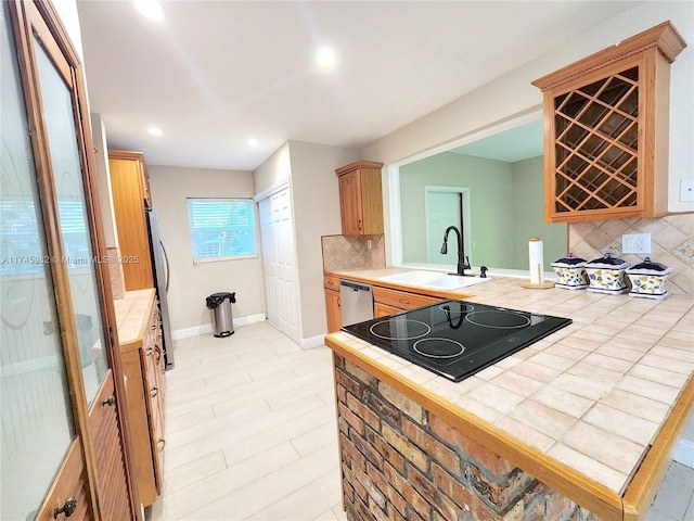 kitchen with tile countertops, stainless steel appliances, a sink, baseboards, and backsplash