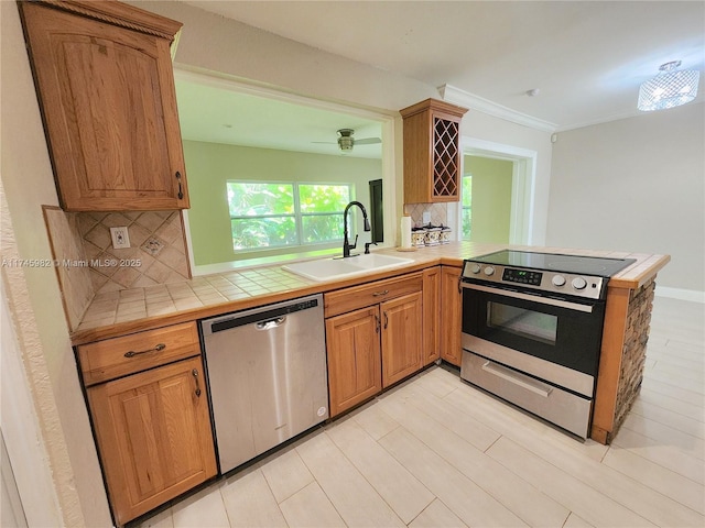 kitchen featuring stainless steel appliances, tile counters, tasteful backsplash, a sink, and a peninsula