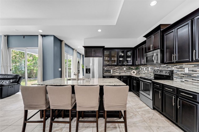 kitchen featuring light stone counters, stainless steel appliances, sink, and a center island with sink