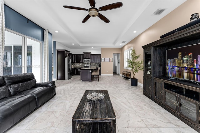 living room with a raised ceiling and ceiling fan