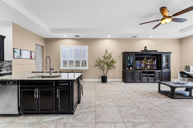 kitchen featuring sink, a tray ceiling, stainless steel dishwasher, and light stone countertops