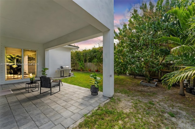 patio terrace at dusk featuring a grill and a lawn