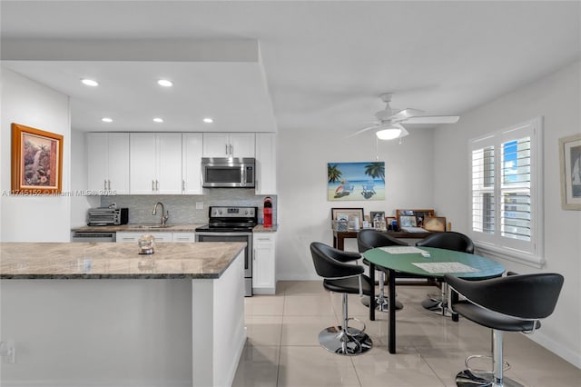 kitchen with light stone counters, tasteful backsplash, light tile patterned floors, appliances with stainless steel finishes, and white cabinets