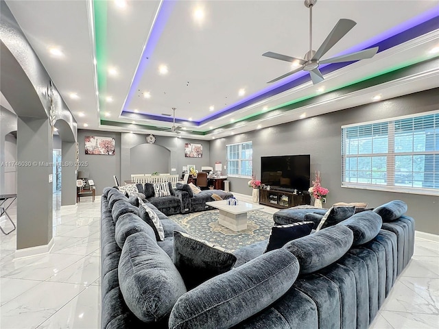 living room with marble finish floor, plenty of natural light, a tray ceiling, and arched walkways