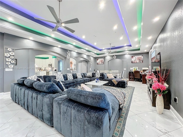 living room featuring marble finish floor, ceiling fan, a tray ceiling, and arched walkways