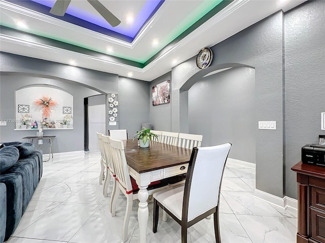 dining room featuring arched walkways, marble finish floor, a raised ceiling, and baseboards