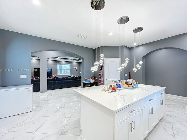 kitchen with arched walkways, a center island, marble finish floor, white cabinetry, and pendant lighting