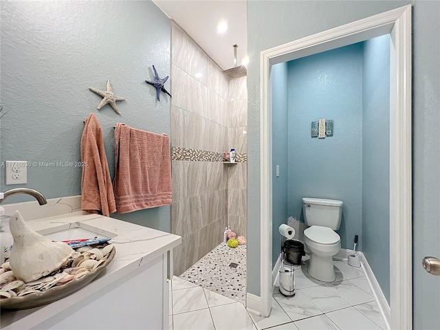 full bathroom with baseboards, tiled shower, vanity, and toilet