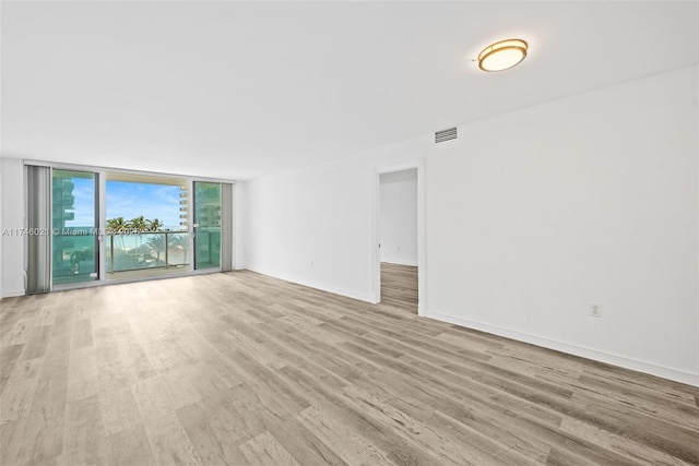 spare room with light wood-style floors, baseboards, expansive windows, and visible vents