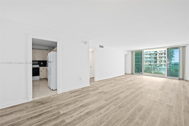 unfurnished living room featuring expansive windows, light wood-style flooring, baseboards, and visible vents