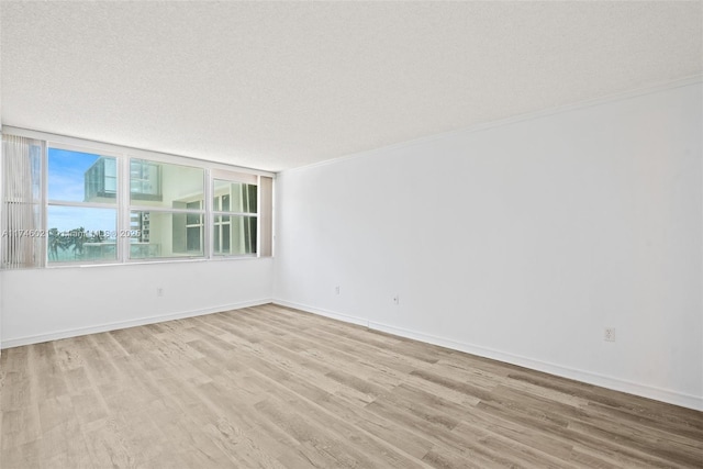 unfurnished room with a textured ceiling, baseboards, ornamental molding, and light wood-type flooring