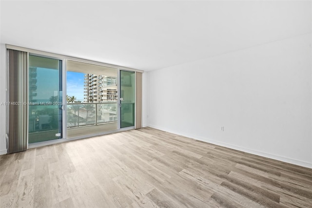 unfurnished room featuring expansive windows, baseboards, and wood finished floors