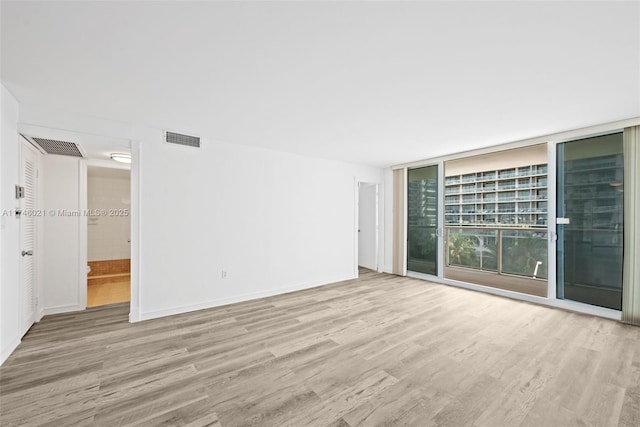 spare room featuring baseboards, floor to ceiling windows, wood finished floors, and visible vents