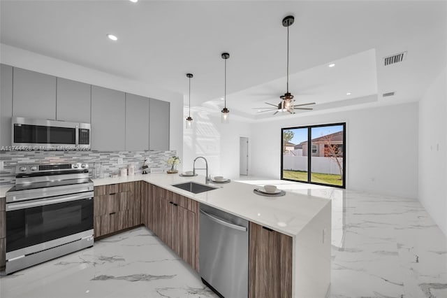 kitchen with sink, appliances with stainless steel finishes, tasteful backsplash, a tray ceiling, and decorative light fixtures