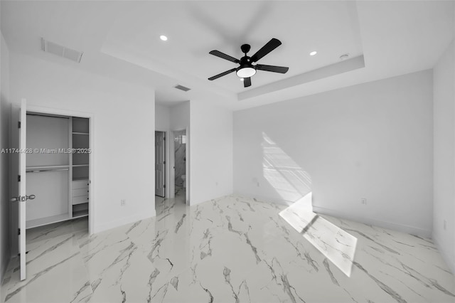 unfurnished bedroom with ensuite bath, ceiling fan, a tray ceiling, a spacious closet, and a closet