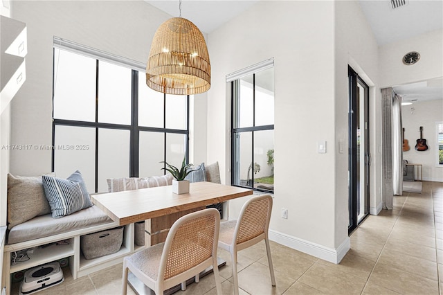 dining room with a towering ceiling, a wealth of natural light, a notable chandelier, and light tile patterned floors