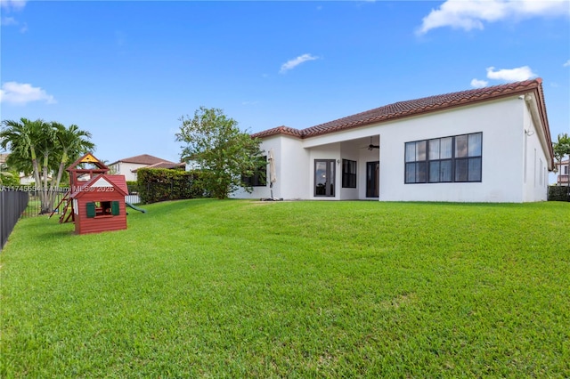 rear view of house with ceiling fan, a yard, and a playground