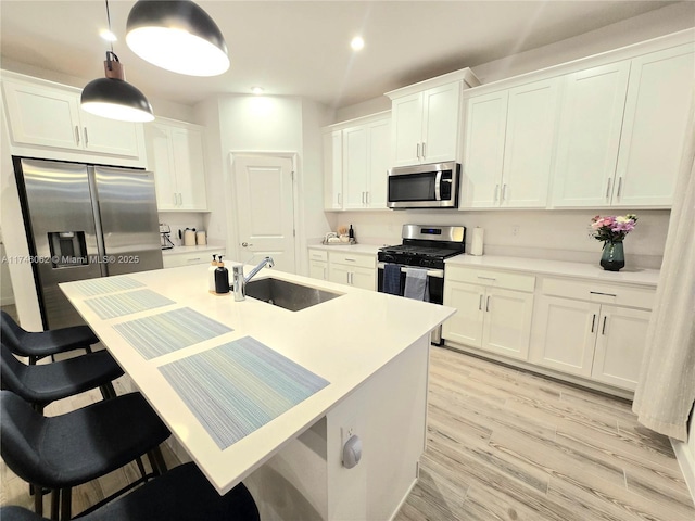 kitchen featuring appliances with stainless steel finishes, sink, white cabinets, a kitchen breakfast bar, and hanging light fixtures