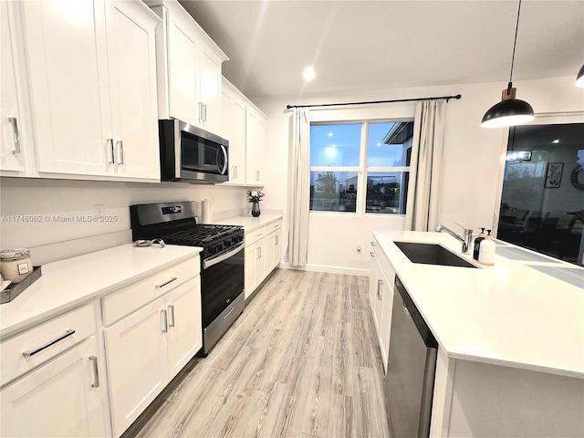 kitchen with sink, decorative light fixtures, light hardwood / wood-style flooring, appliances with stainless steel finishes, and white cabinets