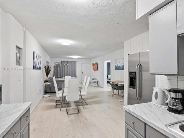 kitchen with gray cabinetry, stainless steel fridge with ice dispenser, a textured ceiling, light wood-type flooring, and light stone countertops