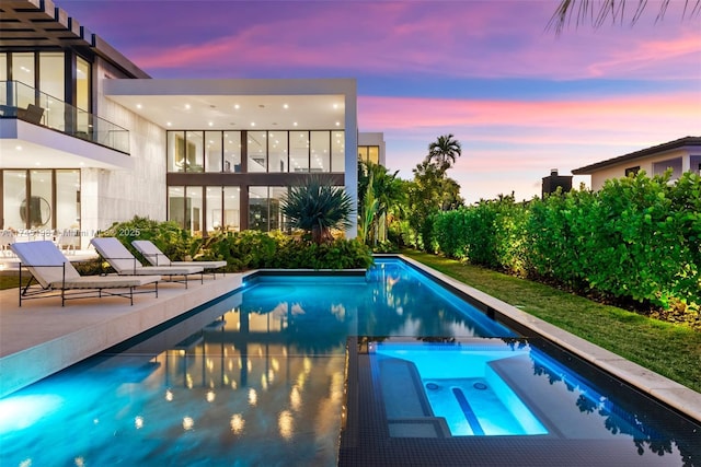 pool at dusk with an in ground hot tub and a patio area