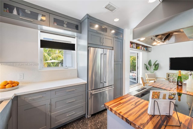 kitchen with high end fridge, wooden counters, vaulted ceiling, gray cabinets, and island exhaust hood