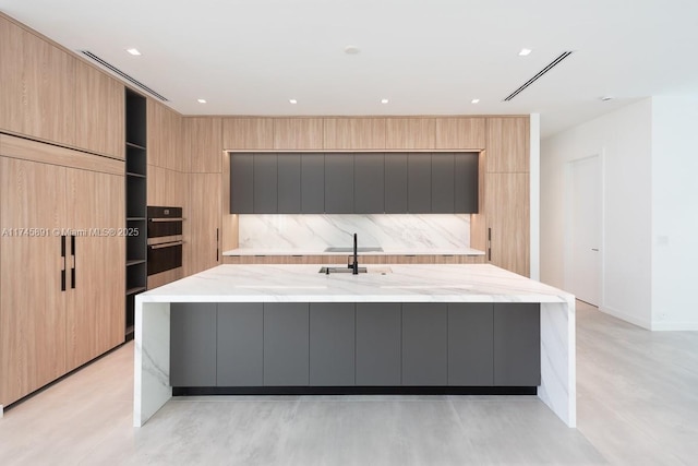 kitchen featuring light stone countertops, sink, light brown cabinets, and a spacious island