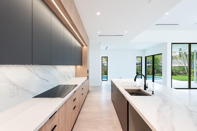 kitchen featuring sink, light stone counters, light brown cabinets, black electric cooktop, and backsplash