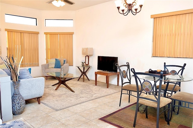 living area with ceiling fan with notable chandelier, light tile patterned floors, a high ceiling, and baseboards