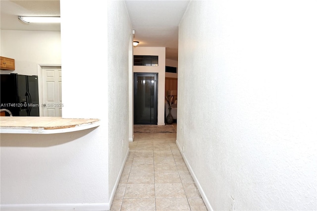 hallway featuring light tile patterned floors, baseboards, and a textured wall