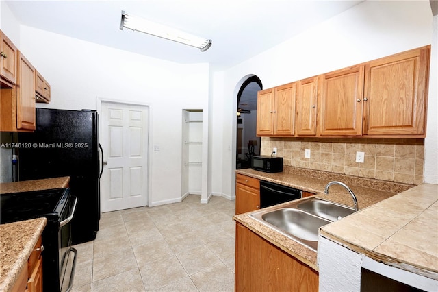 kitchen with brown cabinets, tasteful backsplash, light countertops, a sink, and black appliances