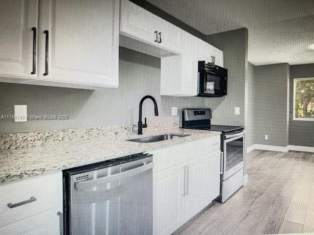 kitchen featuring stainless steel electric range oven, sink, white cabinets, and light stone counters