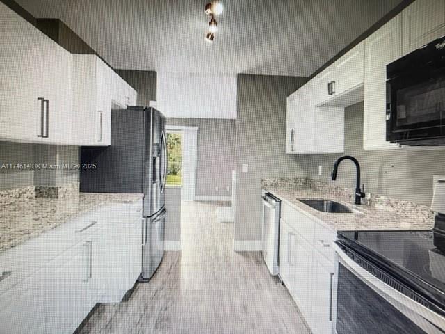 kitchen featuring sink, dishwasher, white cabinetry, stove, and light stone countertops