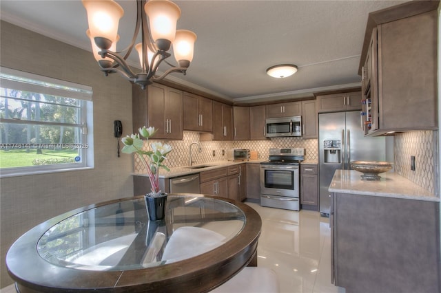 kitchen featuring appliances with stainless steel finishes, decorative light fixtures, sink, ornamental molding, and light stone counters