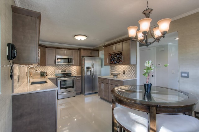 kitchen featuring sink, crown molding, stainless steel appliances, light stone countertops, and decorative light fixtures