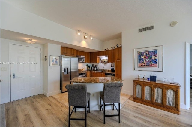 kitchen with a kitchen bar, sink, light hardwood / wood-style flooring, dark stone countertops, and appliances with stainless steel finishes