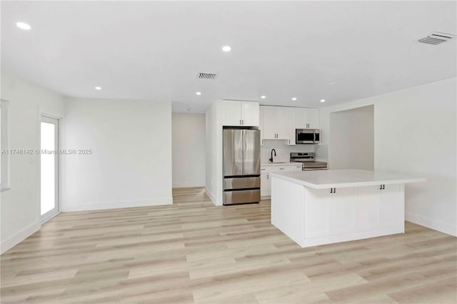 kitchen featuring a kitchen island, appliances with stainless steel finishes, a breakfast bar, white cabinets, and light hardwood / wood-style floors