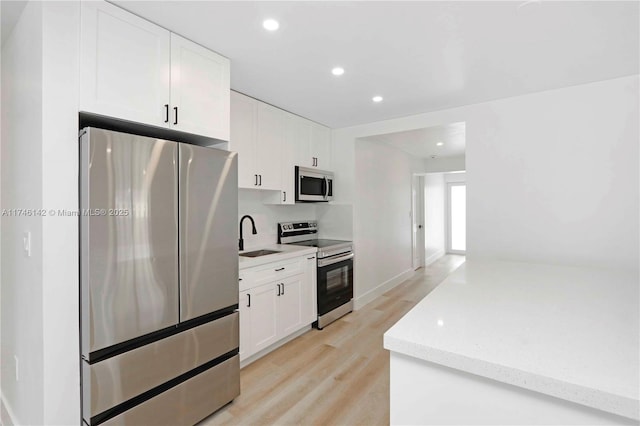 kitchen with appliances with stainless steel finishes, sink, white cabinets, light stone counters, and light hardwood / wood-style floors