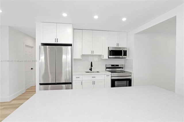 kitchen with sink, light wood-type flooring, white cabinets, and appliances with stainless steel finishes